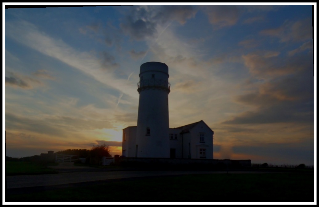 a sunset shining out behind a dark silhouetted lighthouse