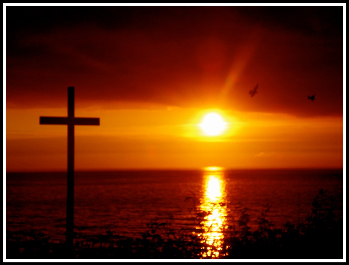 A sunset with streaking light down the centre, a cross on the left and a couple of birds on the right. Taken from a cliff walk.