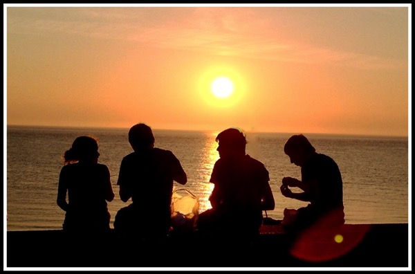 4 people sat on the beach wall with a beautiful sunset around them